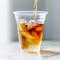 Cold brew being poured into clear cup with ice, sparkling water and orange slice.