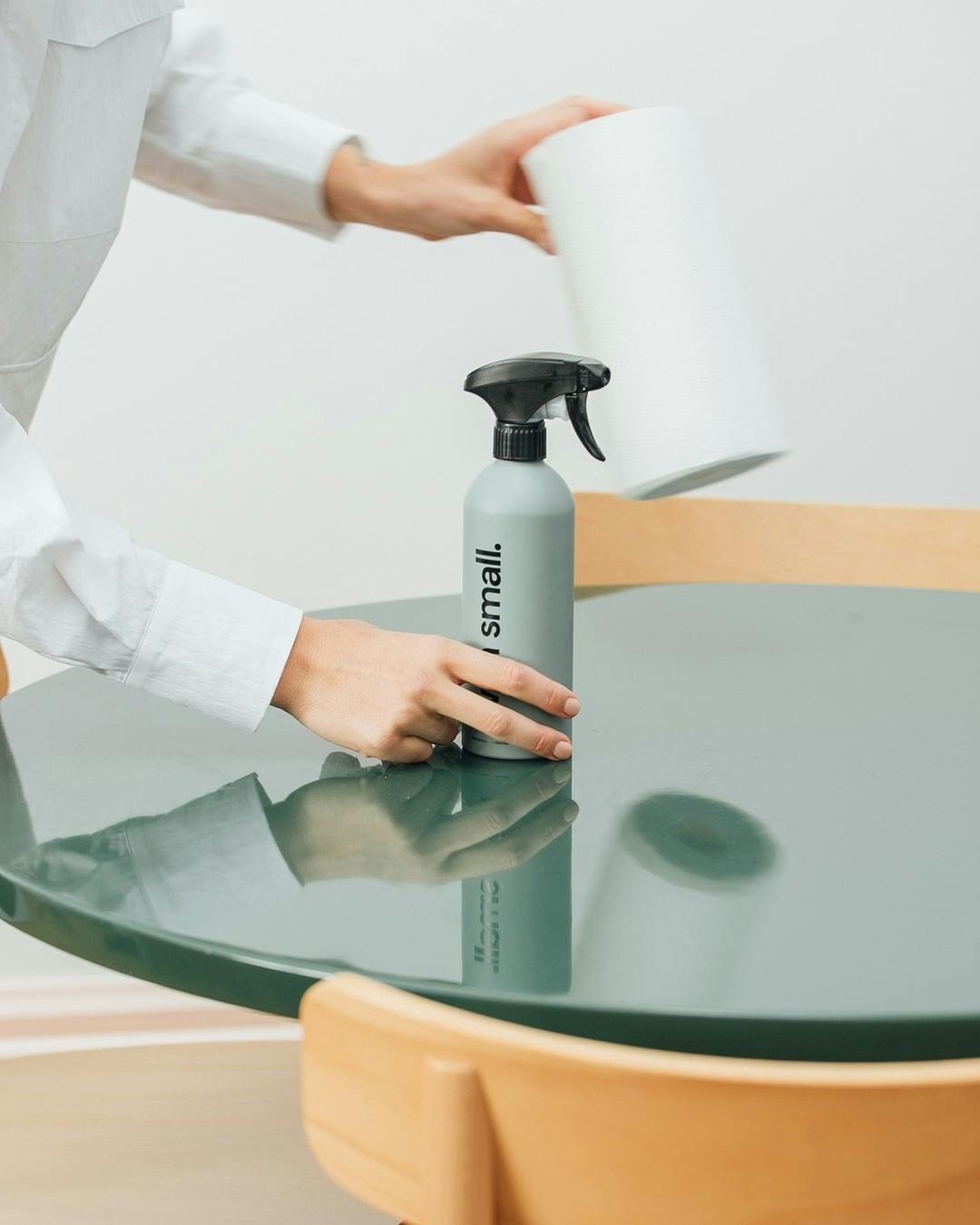 Hands grabbing green With Small spray bottle and paper towels off of a green table